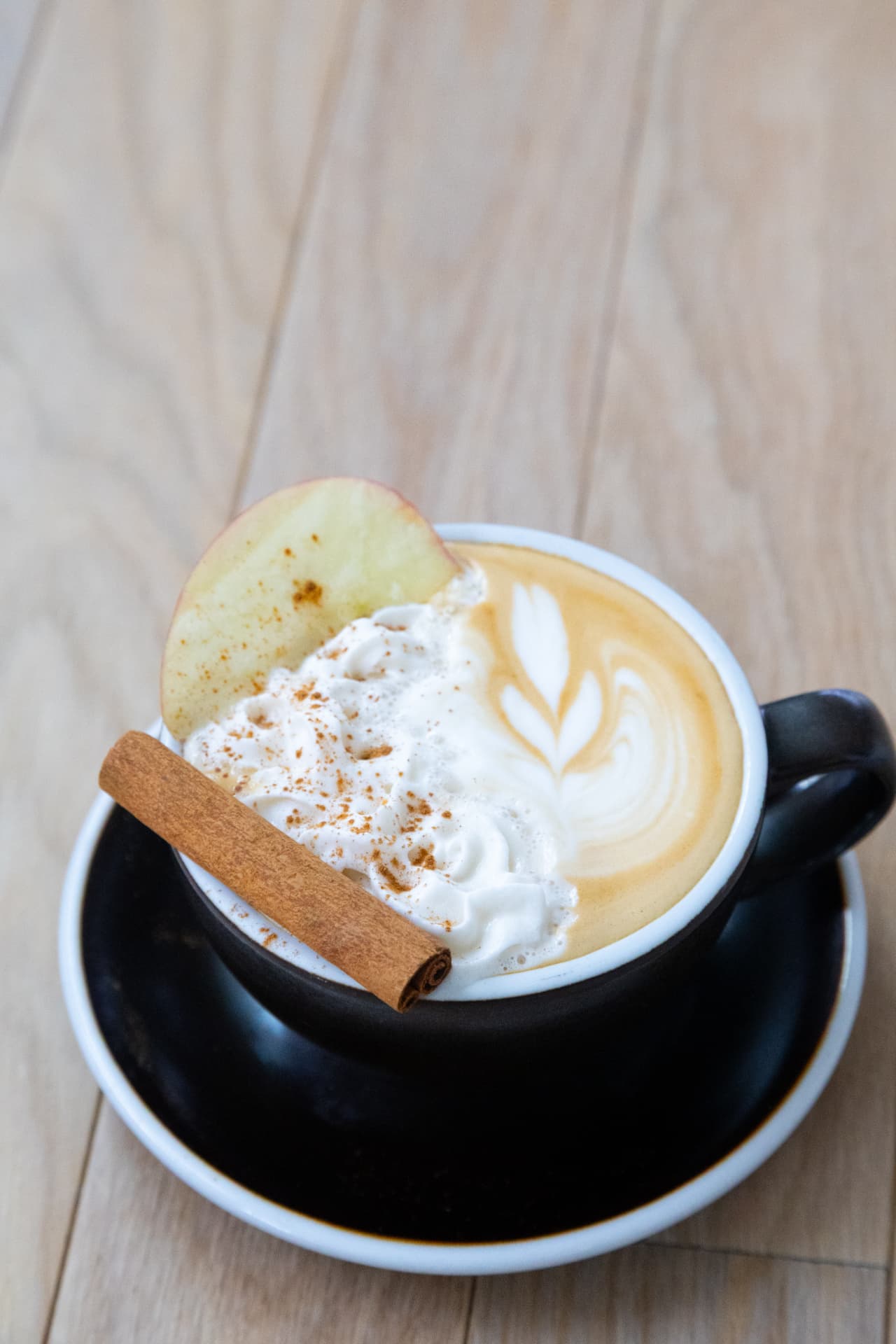 DUO Apple Crisp Latte with an apple slice, whipped cream, latte art and a cinnamon stick